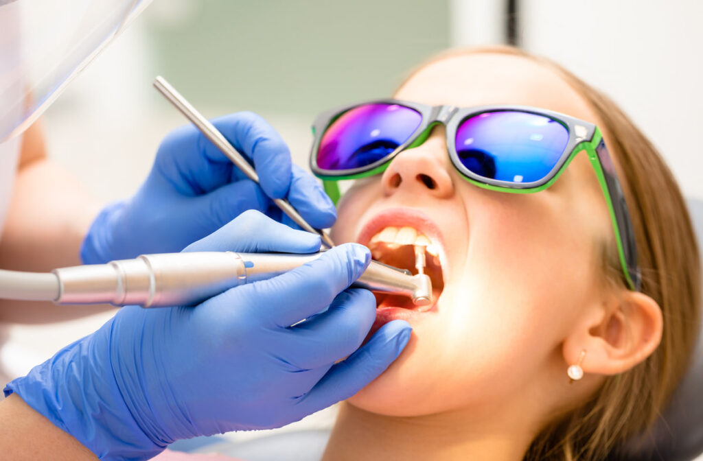 Dental hygienist performing teeth polishing procedure to preteen girl in pediatric dental clinic. Doctor using prophy brush on handpiece to remove hardened deposits of mineralized plaque or tartar