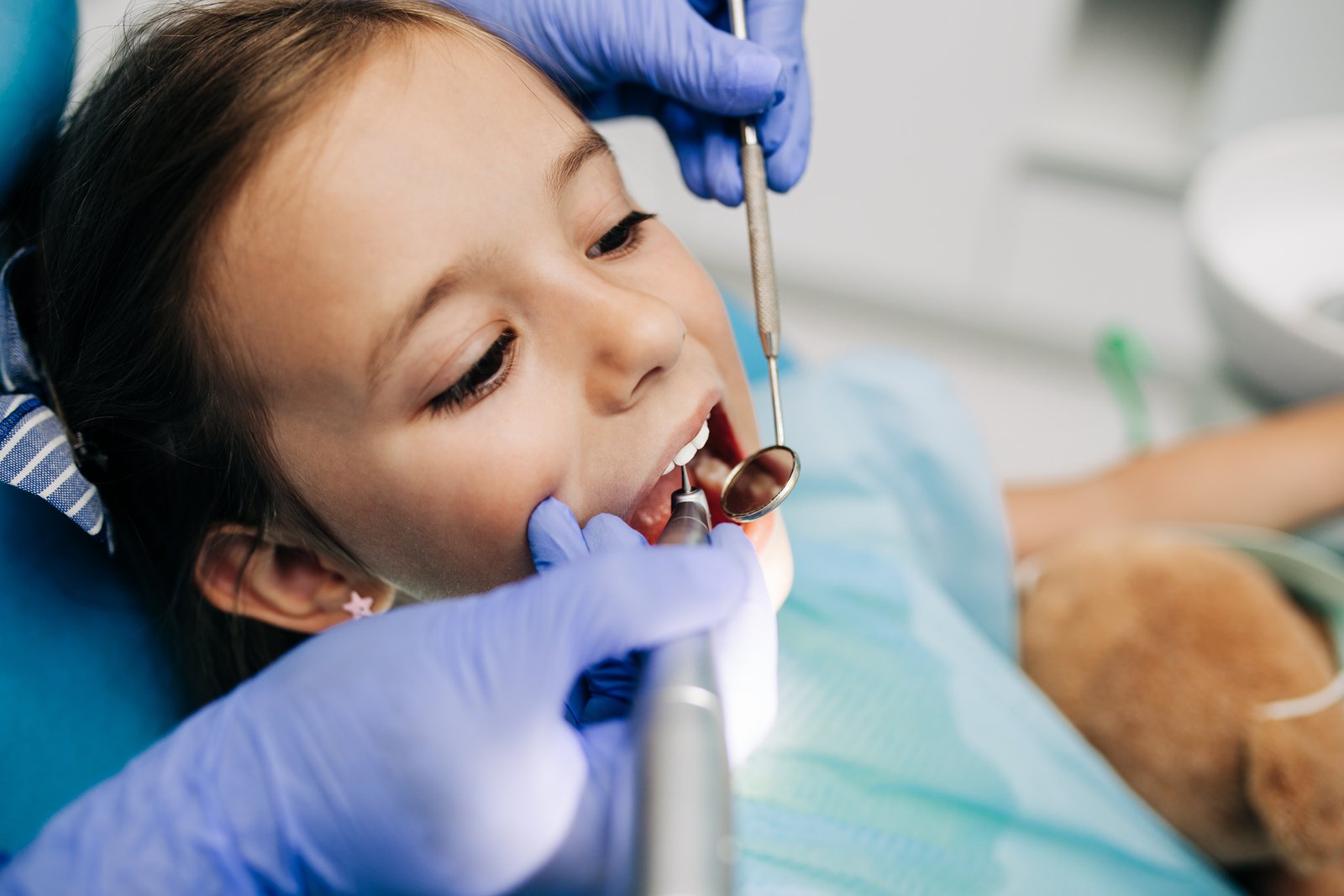 Pediatric dentist examining a child's teeth during a dental crown appointment