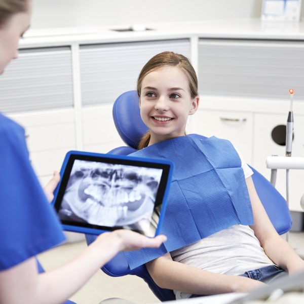 people, medicine, stomatology, technology and health care concept - happy female dentist with teeth x-ray on tablet pc computer and patient girl at dental clinic office