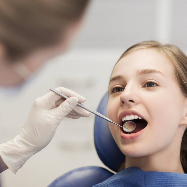 people, medicine, stomatology and health care concept - happy female dentist with mirror checking patient girl teeth up at dental clinic office