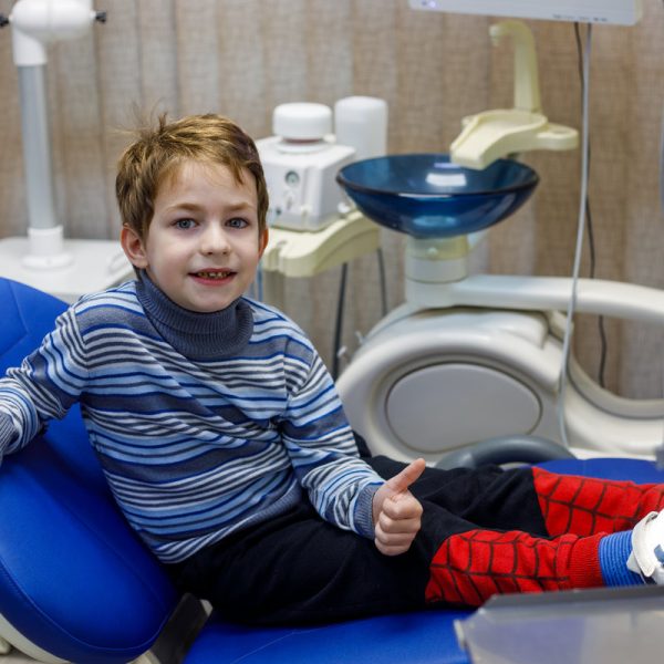 Smiling child sitting in dental chair at modern clinic, pediatric dentistry concept with young patient during dental visit and oral health examination