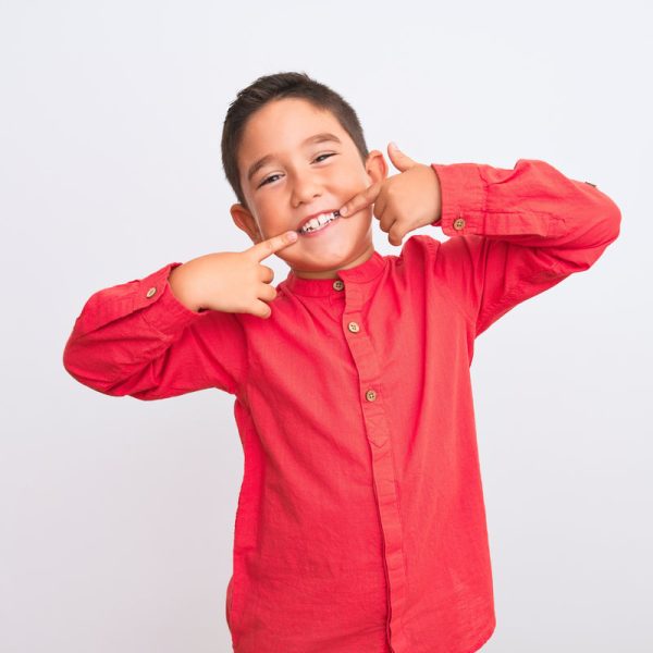Beautiful kid boy wearing elegant red shirt standing over isolated white background smiling cheerful showing and pointing with fingers teeth and mouth. Dental health concept.